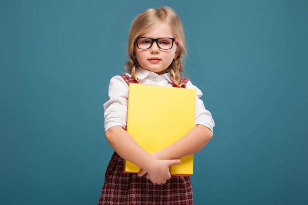 Adorable little girl in red dress, white shirt and glasses holds paper folder