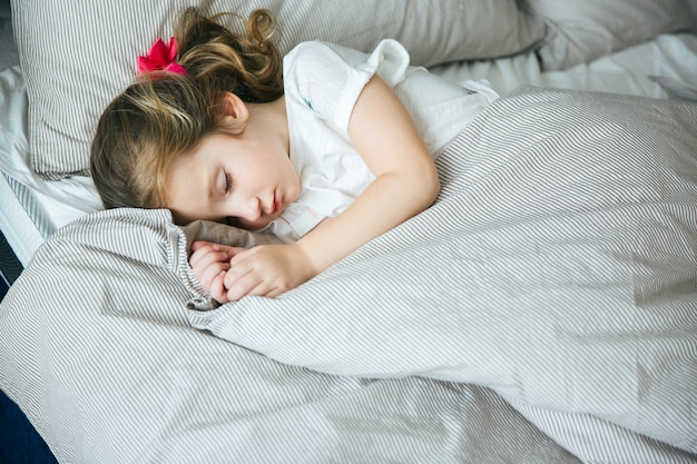 Adorable little girl sleeping in the bed in pajamas under the blanket at home, calm and peaceful