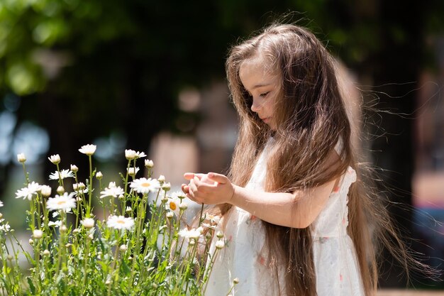 Adorable little girl with beautiful hair playing near flowers in park summertime