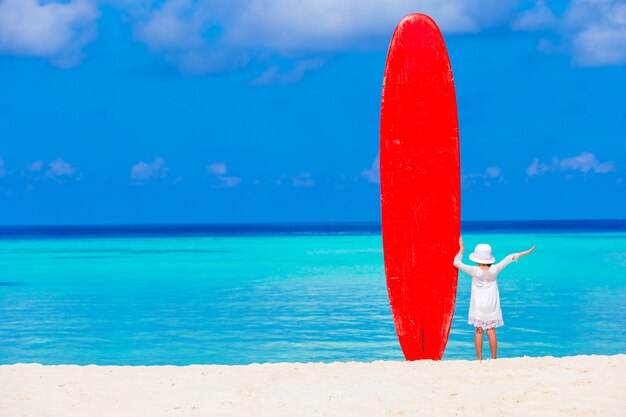 Adorable little girl with big surfboard during tropical vacation