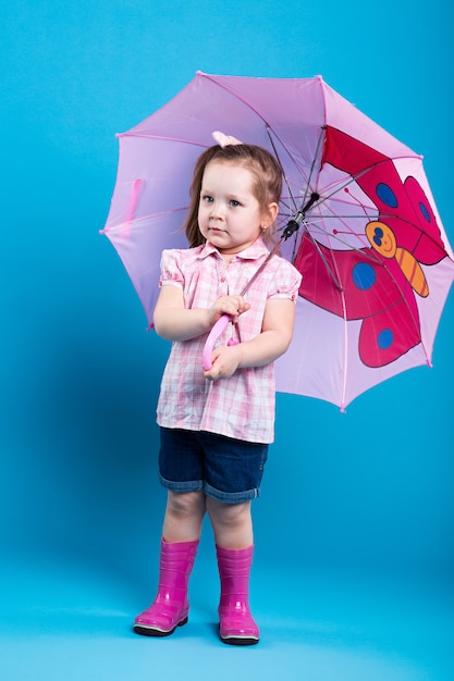 Adorable little girl with pink umbrella on blue background