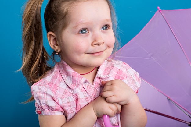 Adorable little girl with pink umbrella on blue background