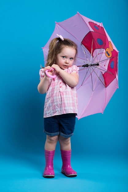 Adorable little girl with pink umbrella on blue background