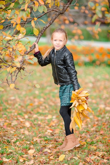 Adorable little girl with yellow leaves bouquet in fall on scooter