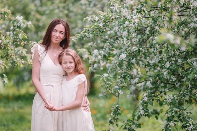 Adorable little girl with young mother in blooming cherry garden on beautiful spring day