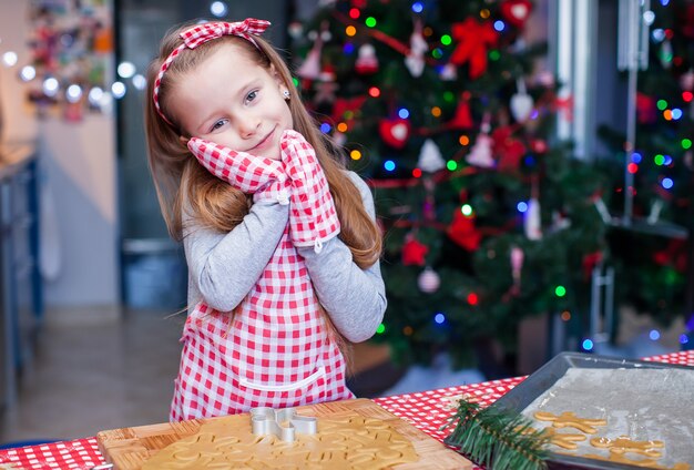 Adorable little girl in wore mittens baking Christmas gingerbread cookies