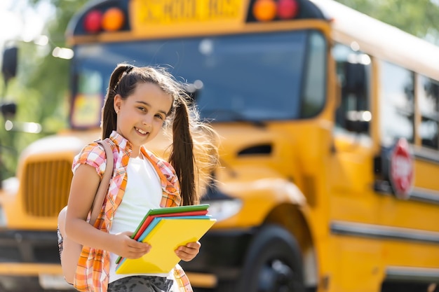 adorable little schoolgirl near school bus and looking at camera