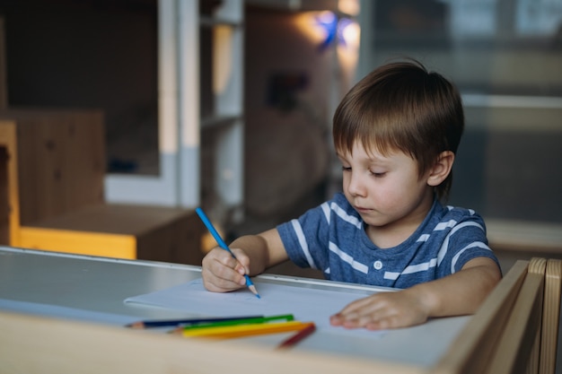 Adorable little toddler boy passionately drawing with color pencils image with selective focus