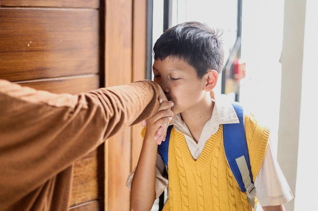 Adorable school boy wearing uniform kiss mother hands going to school, back to school concept.