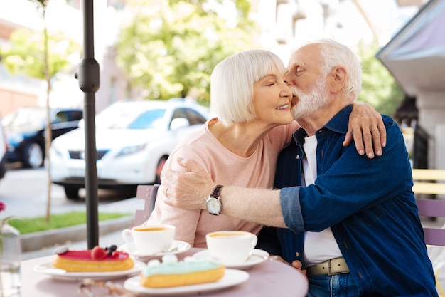 Adorable senior couple exchanging kiss and sitting at cafe