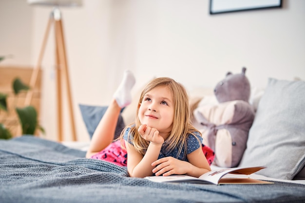 Adorable smiling child reading book while sitting on bed