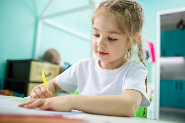 Adorable toddler girl drawing with pencils at home sitting at the table. Creative child sitting in a room learning to draw. Toddler girl doing homework at home.