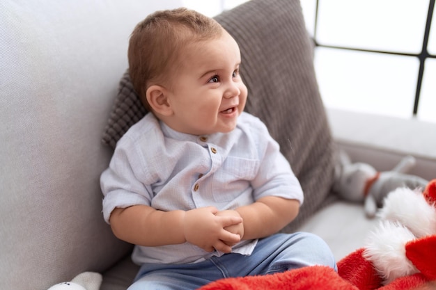 Adorable toddler smiling confident sitting on sofa with christmas hat at home