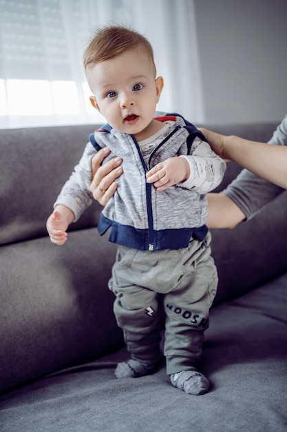 Adorable toddler standing on couch with the help of his mother.