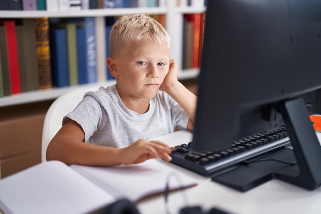 Adorable toddler student boring using computer sitting on table at classroom