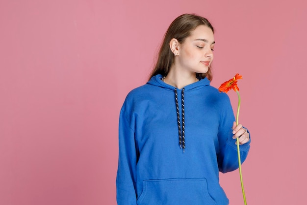 Adorable woman admiring delicate orange gerbera flower on long stem while inhaling aroma