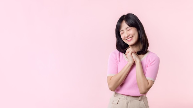 Adorable young happy asian woman model with shy emotion smiling expression cheerful positive attractive face and holding hand isolated on pink pastel studio background Portrait beautiful cute lady