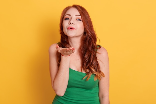 Adorable young woman with long red hair blows kiss