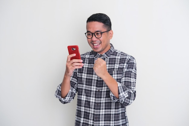 Adult Asian man clenched fist and showing happy expression when looking to his mobile phone