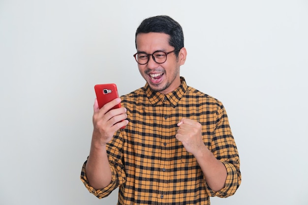 Adult Asian man clenching fist showing excitement when looking to his phone