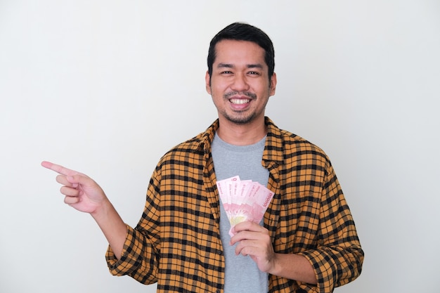 Adult Asian man holding paper money and pointing finger sideways