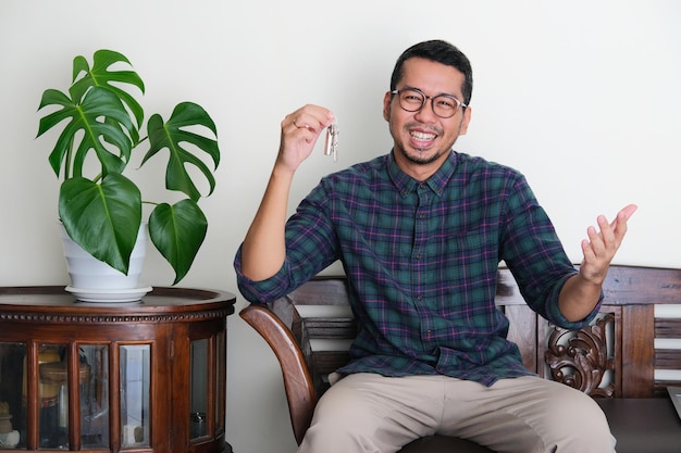 Adult Asian man laughing happy when holding his house key while sitting in a couch