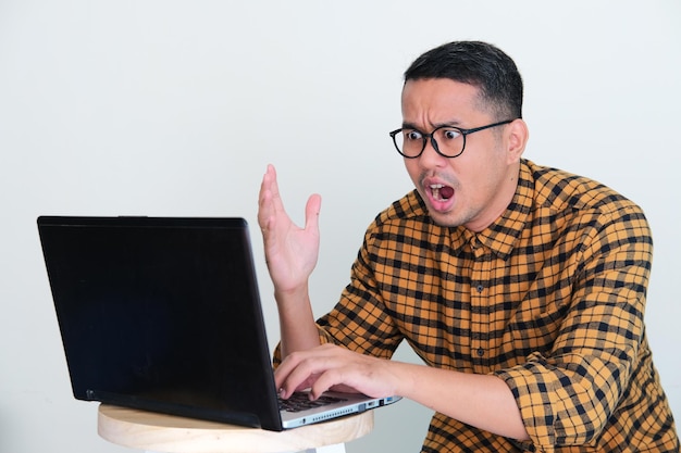 Adult Asian man looking to his laptop with angry expression