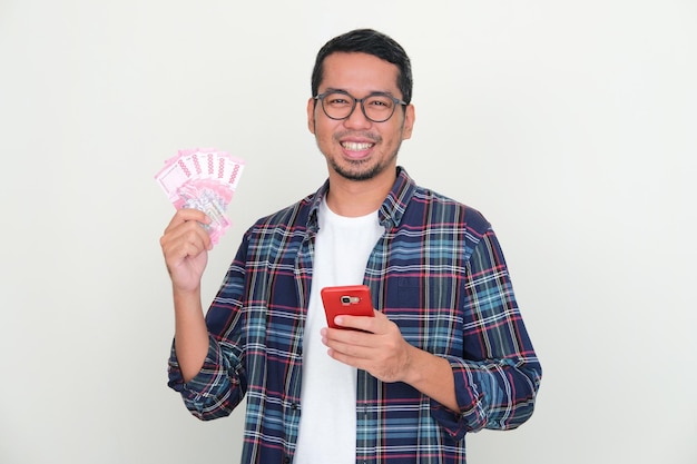 Adult Asian man smiling happy at camera while holding handphone and money