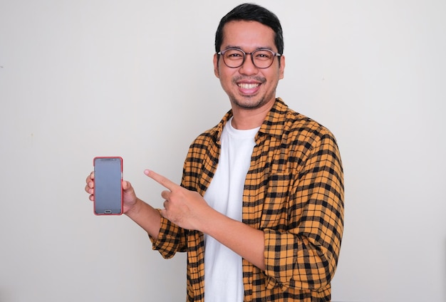 Adult Asian man smiling happy and pointing to blank handphone screen that he hold