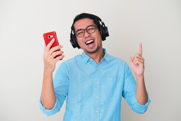 Adult Asian man wearing headset and holding mobile phone while listening to music