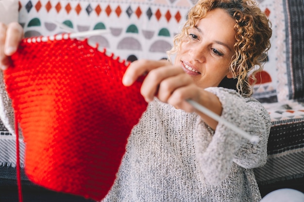 Photo adult attractive woman at home in knitting work activity using colorful wool. happy and relaxed female people enjoying time indoor on the sofa. knit job