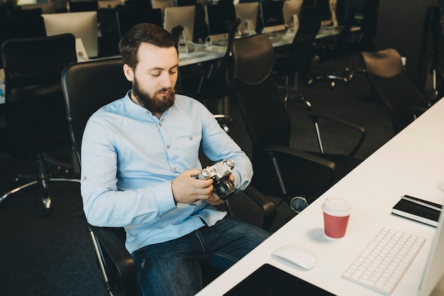 Photo adult bearded man sitting at desk and using photo camera in office