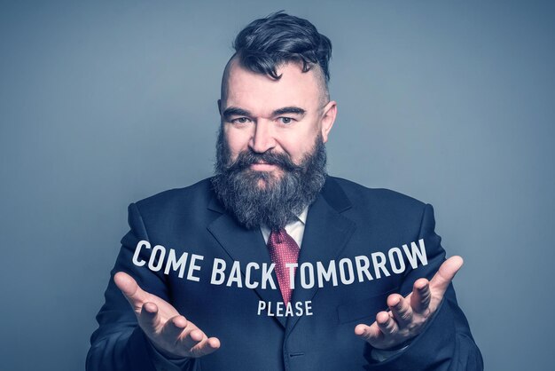 Adult bearded man in a suit holding the inscription COME BACK TOMORROW PLEASE