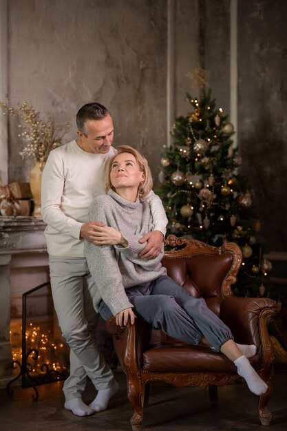 adult beautiful woman and man are sitting on the sofa near the christmas tree