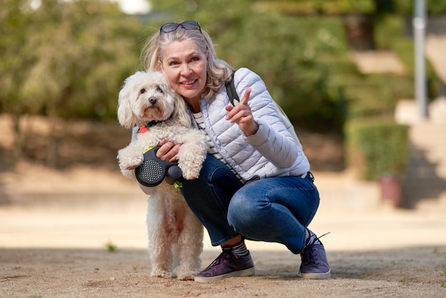 Adult blond woman walking with fluffy white dog in summer city.