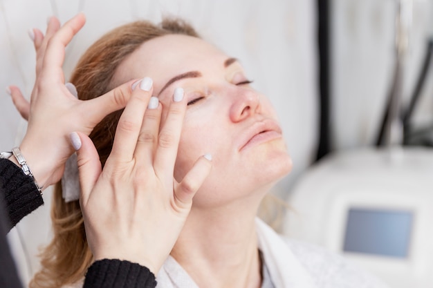 Adult blonde woman apply face cream in a beauty salon. Close-up. Age-related beauty treatments.