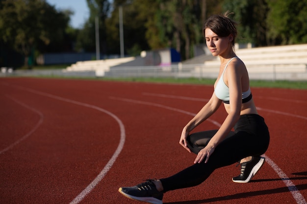 Adult brunette woman in sportswear warms up before sport training at the staduim. Copy space