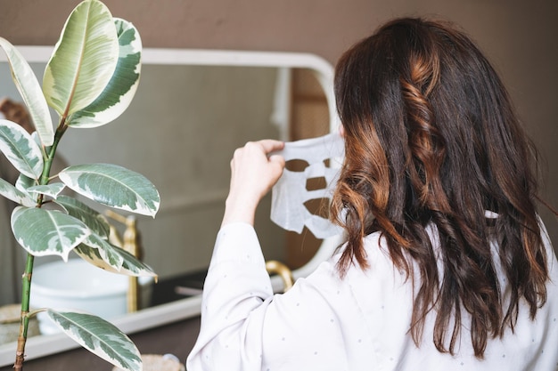 Adult brunette woman with sheet mask on her face in the bathroom at home