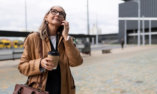 Adult business woman with a cup of coffee talking on the phone outside