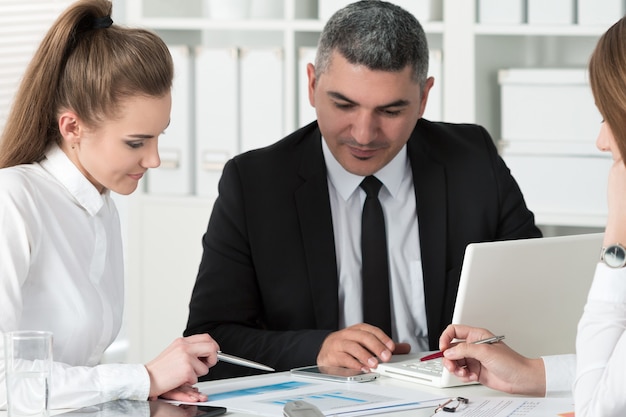 Adult businessman consulting his young female colleague during business meeting. Partners discussing documents and ideas