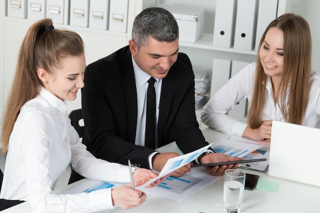 Adult businessman consulting his young female colleagues during business meeting. Partners discussing documents and ideas