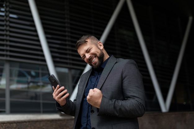 Adult businessman smiling looking at phone screen outside