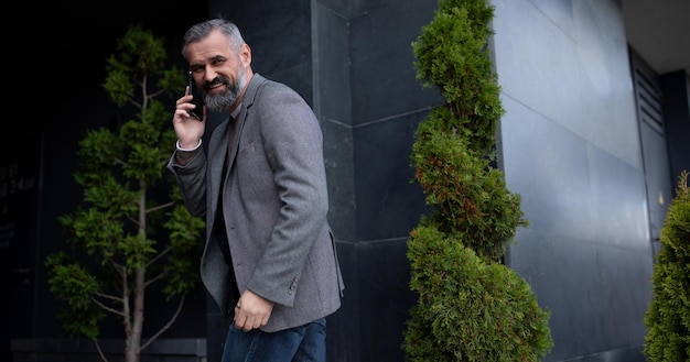 An adult businessman talking on a mobile phone enters turning around the business center building