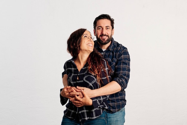 An adult caucasian couple in plaid shirts standing and showing thumbs up to the camera and smiling against a white background.