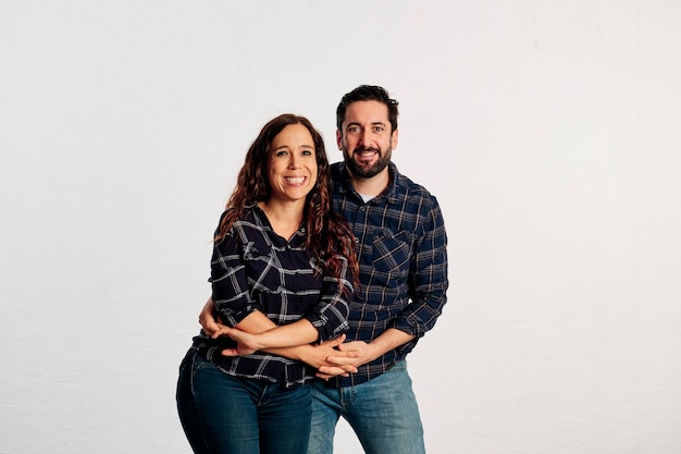 An adult caucasian couple in plaid shirts standing and showing thumbs up to the camera and smiling against a white background.