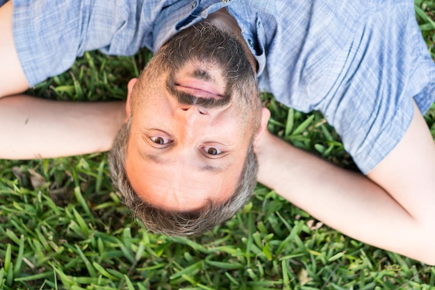 Adult caucasian man lying upside down portrait on grass meadow