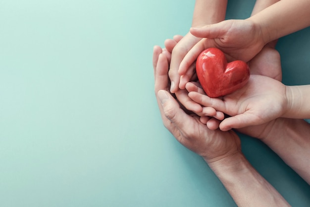 Adult and child hands holding red heart on aqua background