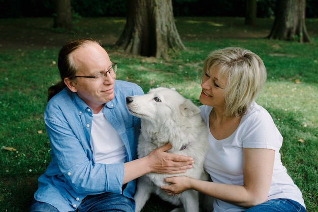 Adult couple sitting on the grass with a white dog