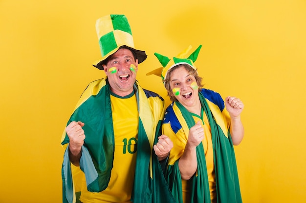 Adult couple soccer fan from brazil wearing flag and hat screaming goal together