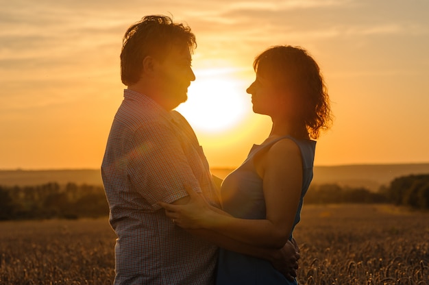 An adult farmer and his wife are hugging in their wheat field.